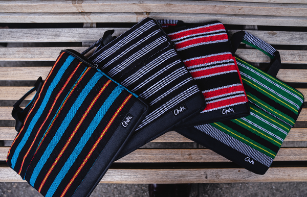 Four laptop bags laying on a bench. First laptop bag is named Siargao and has blue and black stripes. The second laptop bag is all black with white stripes and is named Manila. The third laptop bag has red and black stripes and us is called Davao. The fourth laptop bag has green and black stripes and his called Cebu.
