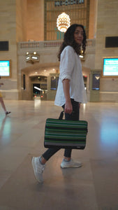A woman walking with a green and black striped laptop bag at Grand Central Station in New York City. The name of the laptop bag is Cebu. 