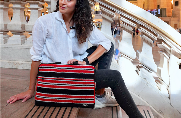 A person sitting with a laptop bag with red, black and white stripes and has handles. The name of the laptop bag is Davao.