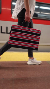 Walking with a red and black laptop bag at a train station in New York City. The name of the laptop bag is Davao. 